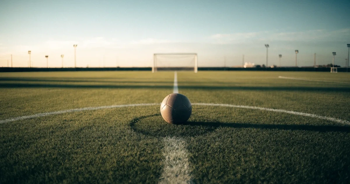 Uma bola de futebol no ponto central de um relvado, à luz da manhã
